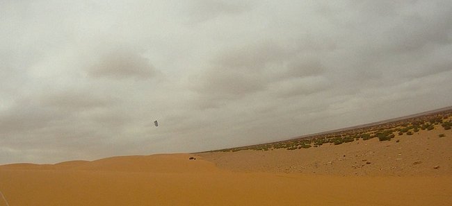 Dunes en bord de pâturage avec au loin un char à cerf-volant au Maroc.