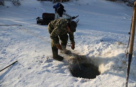 Après avoir percé la glace, Sacha relève le filet lors du voyage à vélo sur le fleuve Amour en Sibérie Après avoir percé la glace, Sacha relève le filet lors du voyage à vélo sur le fleuve Amour en Sibérie