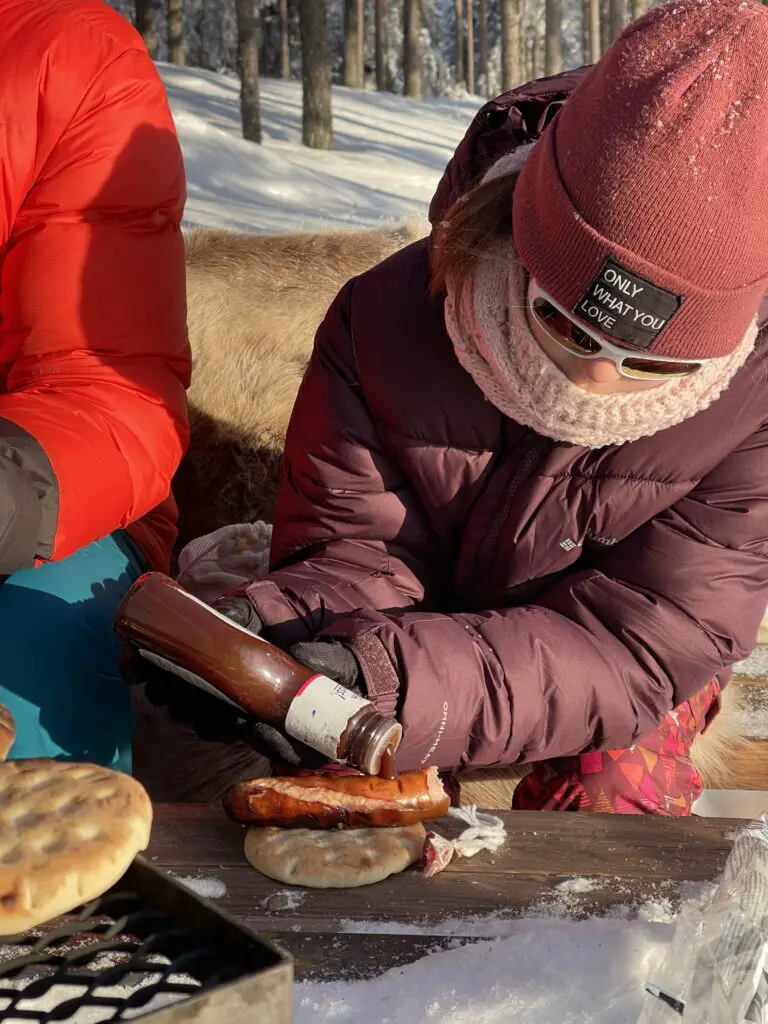 Victoire qui prépare son sandwich saucisse de renne avec du ketchup en laponie